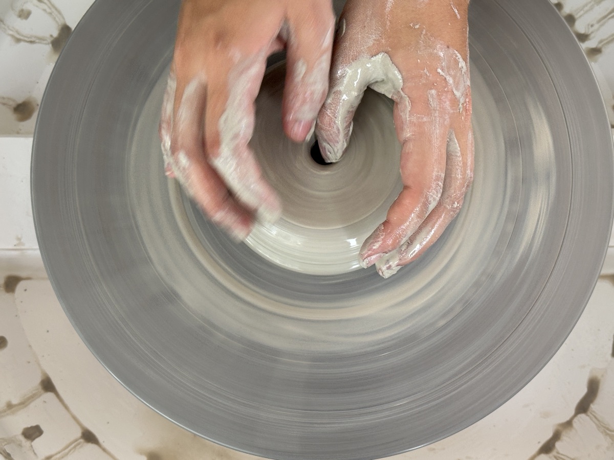 Hands shaping clay on the pottery wheel